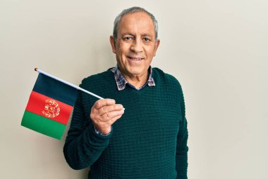 Handsome senior man with grey hair holding afghanistan flag looking positive and happy standing and smiling with a confident smile showing teeth 
