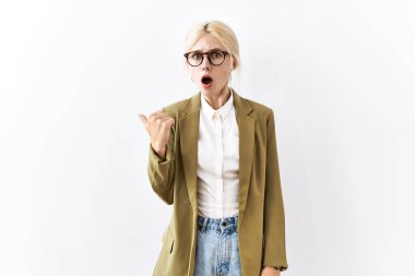 Beautiful caucasian business woman standing over isolated background surprised pointing with hand finger to the side, open mouth amazed expression. 