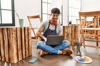 Sanat stüdyosunda kulaklık ve dizüstü bilgisayar kullanan İspanyol genç bir sanatçı..