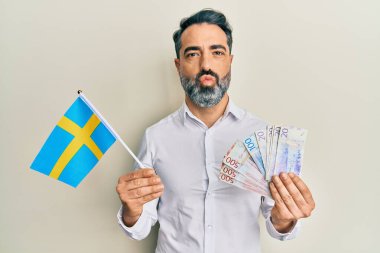 Orta yaşlı, sakallı, gri saçlı, elinde İsveç bayrağı olan ve kameraya bakıp öpüşen sevimli ve seksi bir adam. aşk ifadesi. 