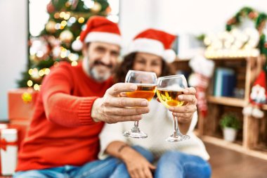 Orta yaşlı İspanyol çift Noel şapkası takıyor. Yerde oturup evde şampanyayla kadeh kaldırıyorum..