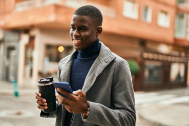 Genç Afrikalı Amerikalı adam akıllı telefon kullanıyor. Şehirde kahve içiyor.