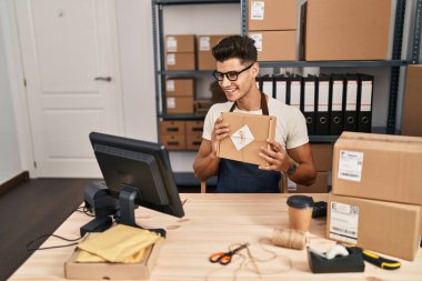 Young hispanic man ecommerce business worker having video call showing package at office