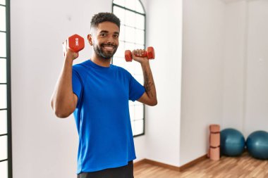 Yakışıklı İspanyol adam spor salonunda egzersiz yapıyor. Elinde dambıllar var.