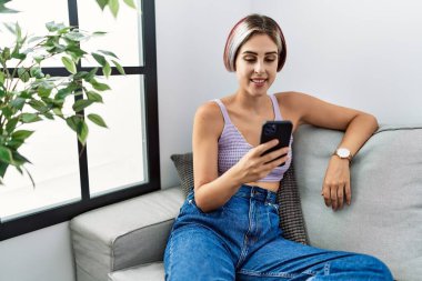 Young beautiful woman using smartphone typing message sitting on the sofa with a happy and cool smile on face. lucky person. 