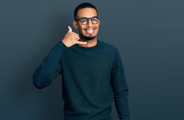 Genç Afro-Amerikan adam günlük kıyafetler ve gözlük takıyor gülümsüyor telefonla el ve parmak hareketleri yapıyor telefonda konuşuyor gibi. iletişim kavramları. 
