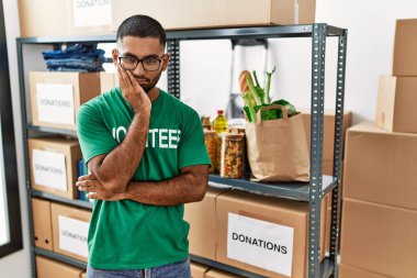 Young indian man volunteer holding donations box thinking looking tired and bored with depression problems with crossed arms. 