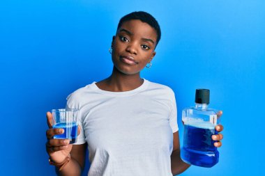 Young african american woman holding mouthwash for fresh breath relaxed with serious expression on face. simple and natural looking at the camera. 
