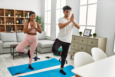 Gülümseyen genç Latin çift evde mutlu yoga pozu veriyor..