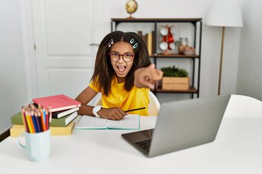 Young african american girl doing homework at home pointing displeased and frustrated to the camera, angry and furious with you 