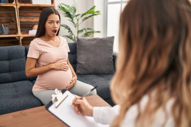 Young pregnant woman at therapy session scared and amazed with open mouth for surprise, disbelief face 