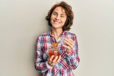 Genç esmer kadın elinde taze bal tutarken yüzünde mutlu ve serin bir gülümsemeyle gülümsüyor. diş gösterme. 