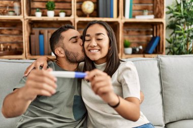 Genç Latin çift gülümsüyor. Mutlu görünüyor. Hamile test sonuçları evde..