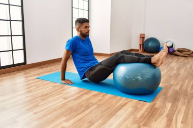 Yakışıklı İspanyol adam egzersiz yapıyor ve yoga minderinde geriniyor, spor salonunda pilates topuyla esneklik gösteriyor.
