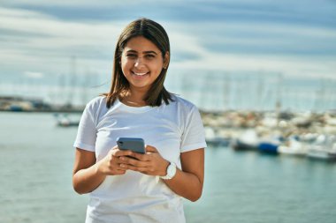 Plajda akıllı telefon kullanarak mutlu gülümseyen genç Latin kız..