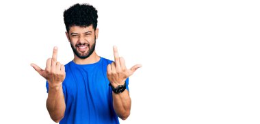 Young arab man with beard wearing casual blue t shirt showing middle finger doing fuck you bad expression, provocation and rude attitude. screaming excited 