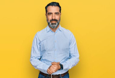 Orta yaşlı, sakallı, iş gömleği giyen, elleri çapraz parmaklı, rahat ve neşeli gülümseyen bir adam. Başarı ve iyimserlik 