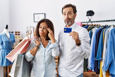 Hispanic middle age couple holding shopping bags and credit card shooting and killing oneself pointing hand and fingers to head like gun, suicide gesture. 