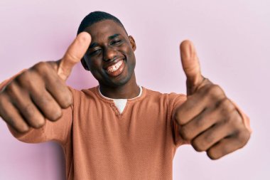 Genç Afro-Amerikan adam günlük giysiler giyip olumlu jestler yapıyor. Elleriyle gülümsüyor ve başarı için seviniyor. kazanan jest. 