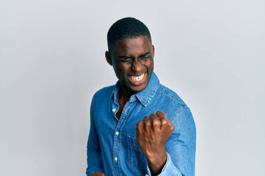 Gündelik giysiler giyen genç Afrikalı Amerikalı adam kolları havada ve gözleri kapalı bir şekilde başarının şaşkınlığını ve şaşkınlığını yaşıyor. 