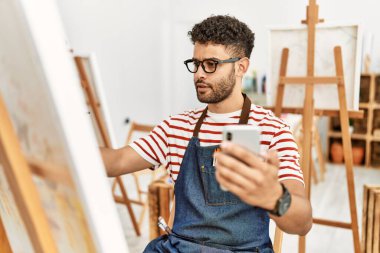 Sanat stüdyosunda akıllı telefon çizimi yapan genç bir Arap sanatçı..