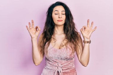 Gündelik kıyafetler giyen, gözleri kapalı gülümseyen genç İspanyol kadın parmaklarıyla meditasyon hareketi yapıyor. yoga konsepti. 