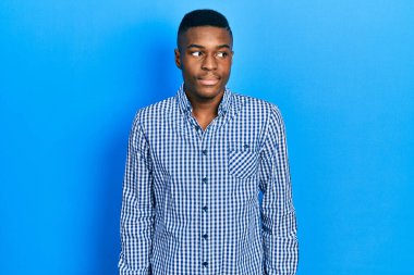 Genç Afro-Amerikan adam günlük kıyafetler giyiyor gülümsüyor yan tarafa bakıyor ve düşünüyor. 