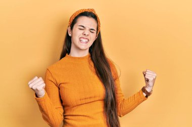 Young brunette teenager wearing casual yellow sweater very happy and excited doing winner gesture with arms raised, smiling and screaming for success. celebration concept. 