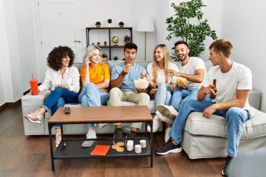 Mutlu bir şekilde gülümseyen bir grup genç arkadaş evde film izliyor..