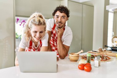 Mutfakta dizüstü bilgisayar kullanarak mutlu gülümseyen genç çift..
