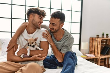 İki İspanyol erkek yatak odasında Chihuahua ile yatakta birbirlerine sarılıyorlar.