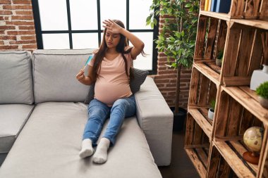 Evdeki kanepede el yelpazesiyle oturan genç Latin kadın hamile.