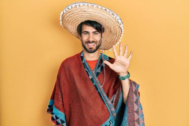 Young hispanic man holding mexican hat showing and pointing up with fingers number five while smiling confident and happy. 