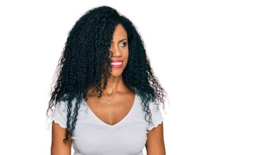 Middle age african american woman wearing casual white t shirt looking away to side with smile on face, natural expression. laughing confident. 
