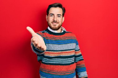 Handsome caucasian man with beard wearing elegant wool winter sweater smiling friendly offering handshake as greeting and welcoming. successful business. 