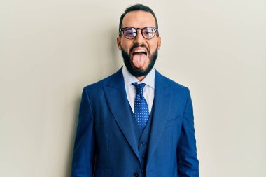 Young man with beard wearing business suit and tie sticking tongue out happy with funny expression. emotion concept. 