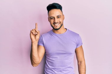 Gündelik giysiler giymiş genç bir Arap başarılı bir fikirle işaret ediyor. Heyecanlı ve mutlu. Bir numara.. 