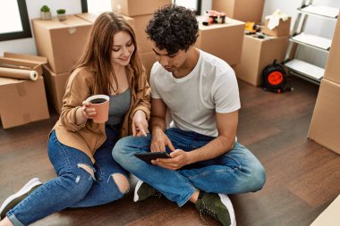 Genç çift mutlu bir şekilde dokunmatik ped kullanıyor ve yeni evlerinde kahve içiyor..