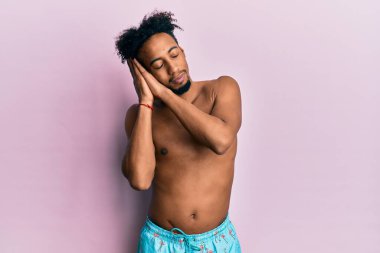 Young african american man with beard wearing swimsuit sleeping tired dreaming and posing with hands together while smiling with closed eyes. 