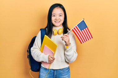 Young chinese girl exchange student holding america flag smiling with a happy and cool smile on face. showing teeth. 