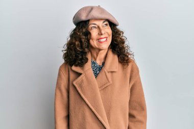 Middle age hispanic woman wearing french look with beret looking away to side with smile on face, natural expression. laughing confident. 
