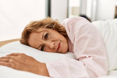 Orta yaşlı beyaz kadın yatak odasında yatakta yatıyor..