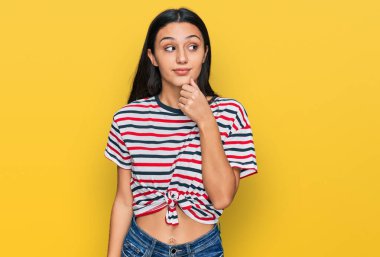 Elleri çenesinde gündelik giysiler içinde soru soran genç İspanyol kız, düşünceli ifade. Düşünceli bir yüzle gülümsüyor. şüphe kavramı. 