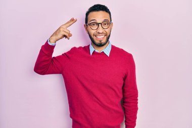Hispanic man with beard wearing business shirt and glasses shooting and killing oneself pointing hand and fingers to head like gun, suicide gesture. 