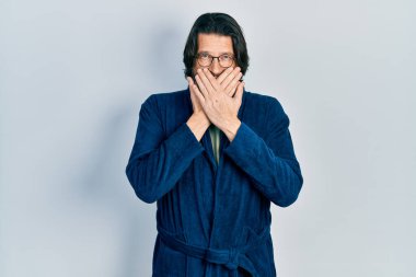 Middle age caucasian man wearing bathrobe and glasses shocked covering mouth with hands for mistake. secret concept. 