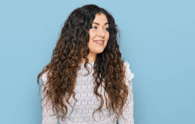 Günlük kıyafetler giyen genç İspanyol kız yüzünde gülümsemeyle yan yana bakıyor, doğal bir ifade. Kendinden emin gülen. 