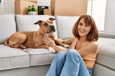 Beyaz bir kadın köpeğe sarılıyor. Evde yerde oturuyor.