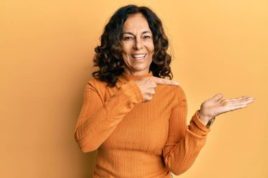 Orta yaşlı İspanyol kadın gündelik giysiler giyip kameraya hayret ediyor ve gülümsüyor.. 