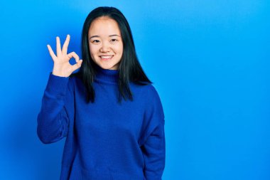 Young chinese girl wearing casual clothes smiling positive doing ok sign with hand and fingers. successful expression. 