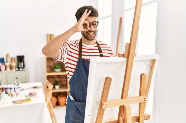 Sanat stüdyosundaki Arap genç adam el hareketleriyle gülümsüyor ve mutlu yüzüyle parmaklarının arasından bakıyor.. 